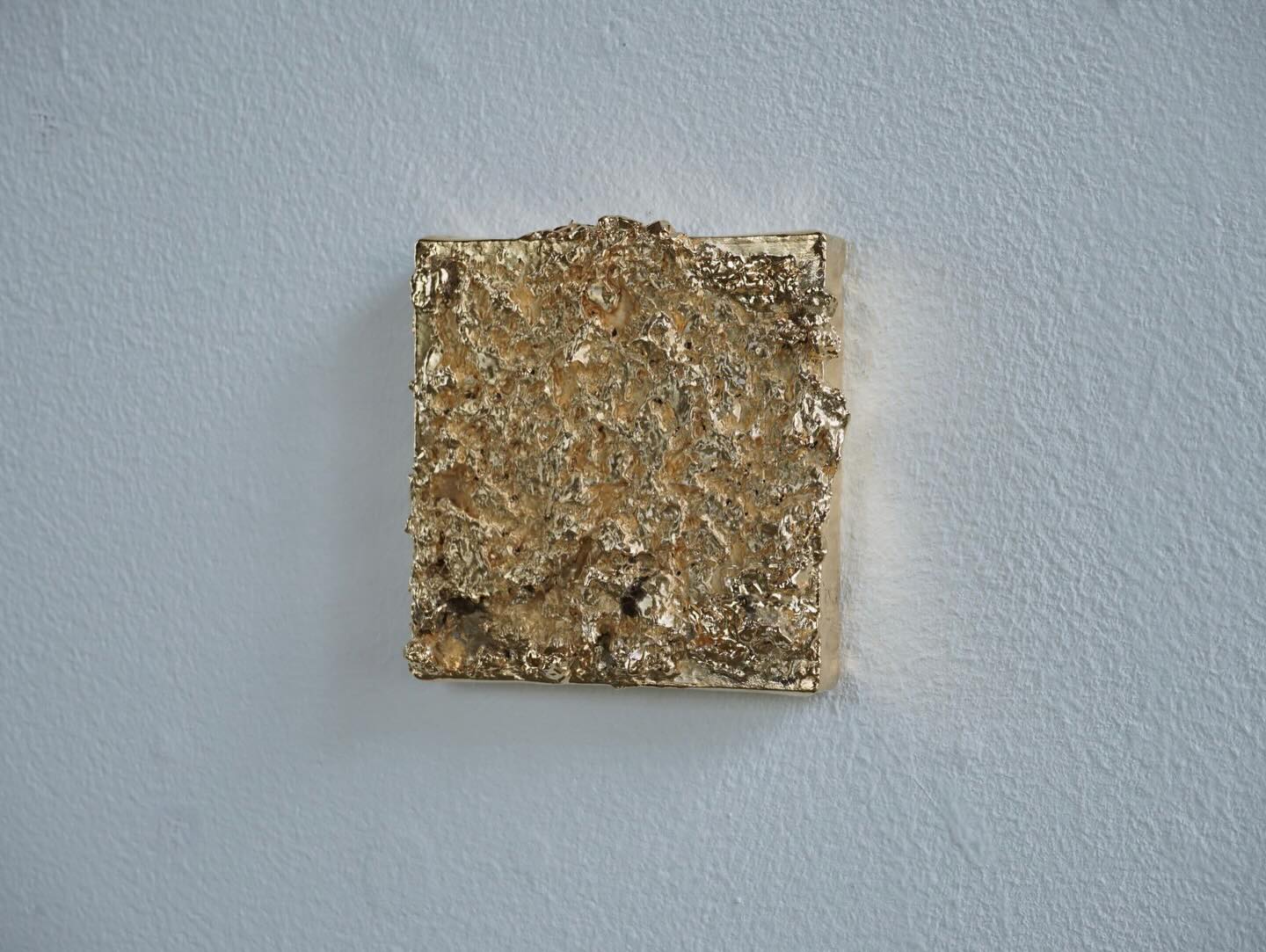 A small reflective gold-toned textured cast mounted on a white wall