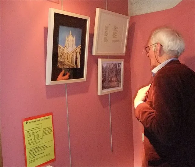 A visitor looking closely at framed work installed on a red exhibition wall